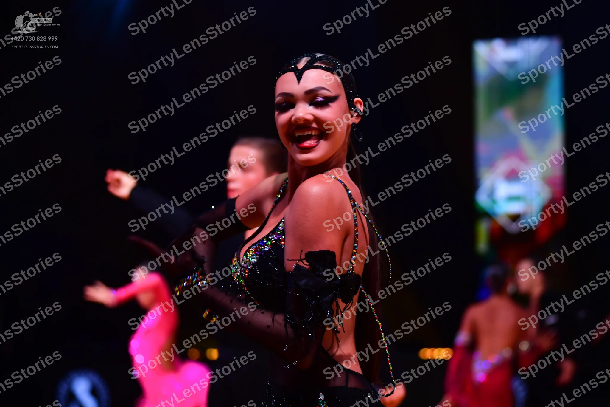 Dancesport competitor: Female dancer in foreground: black latin dress with sequins and sheer, embellish