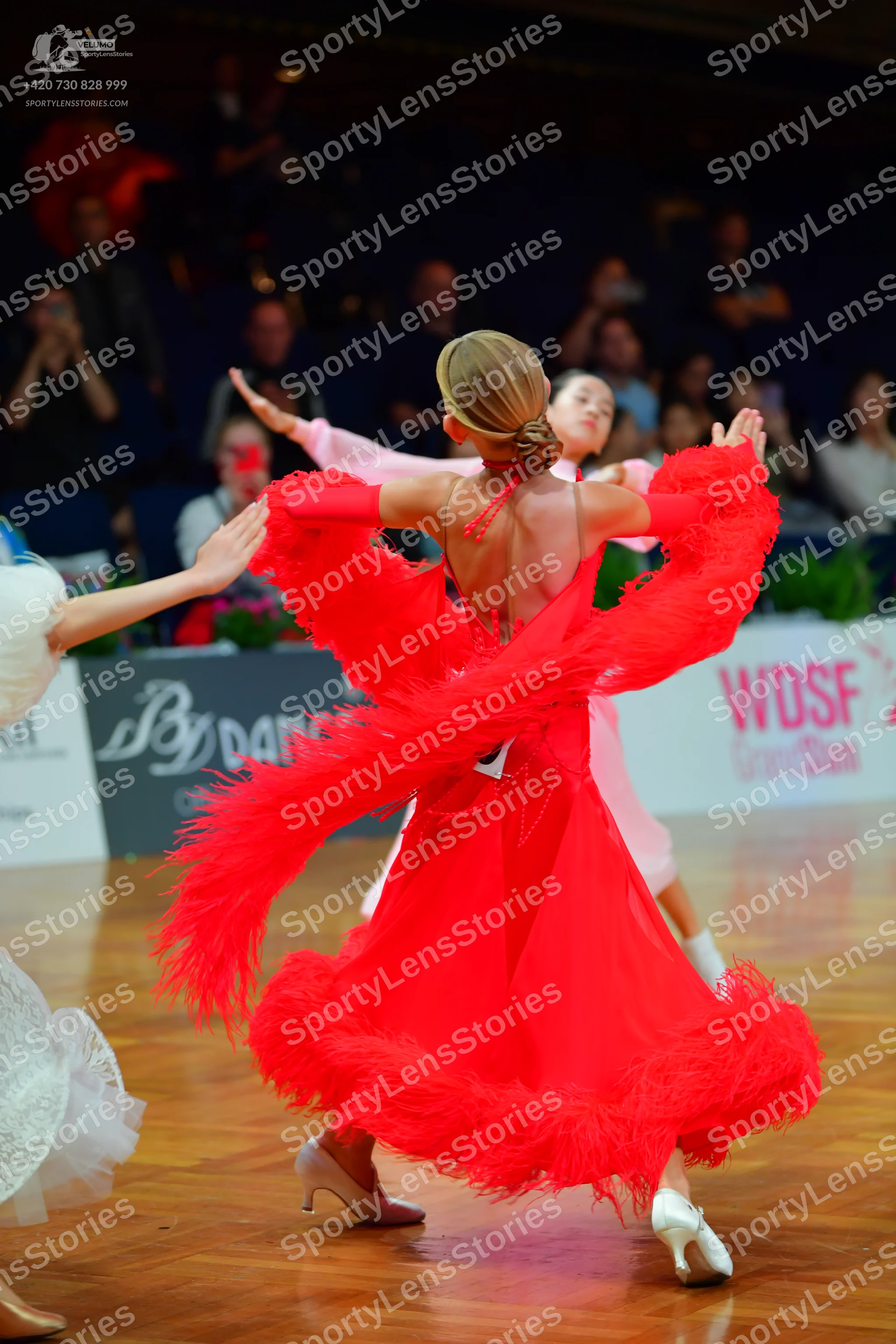 Dancesport competitor: Female dancer in foreground: red Latin dress with voluminous red feather-like fr