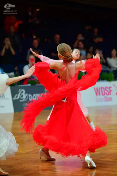 Dancesport competitor: Female dancer in foreground: red Latin dress with voluminous red feather-like fr