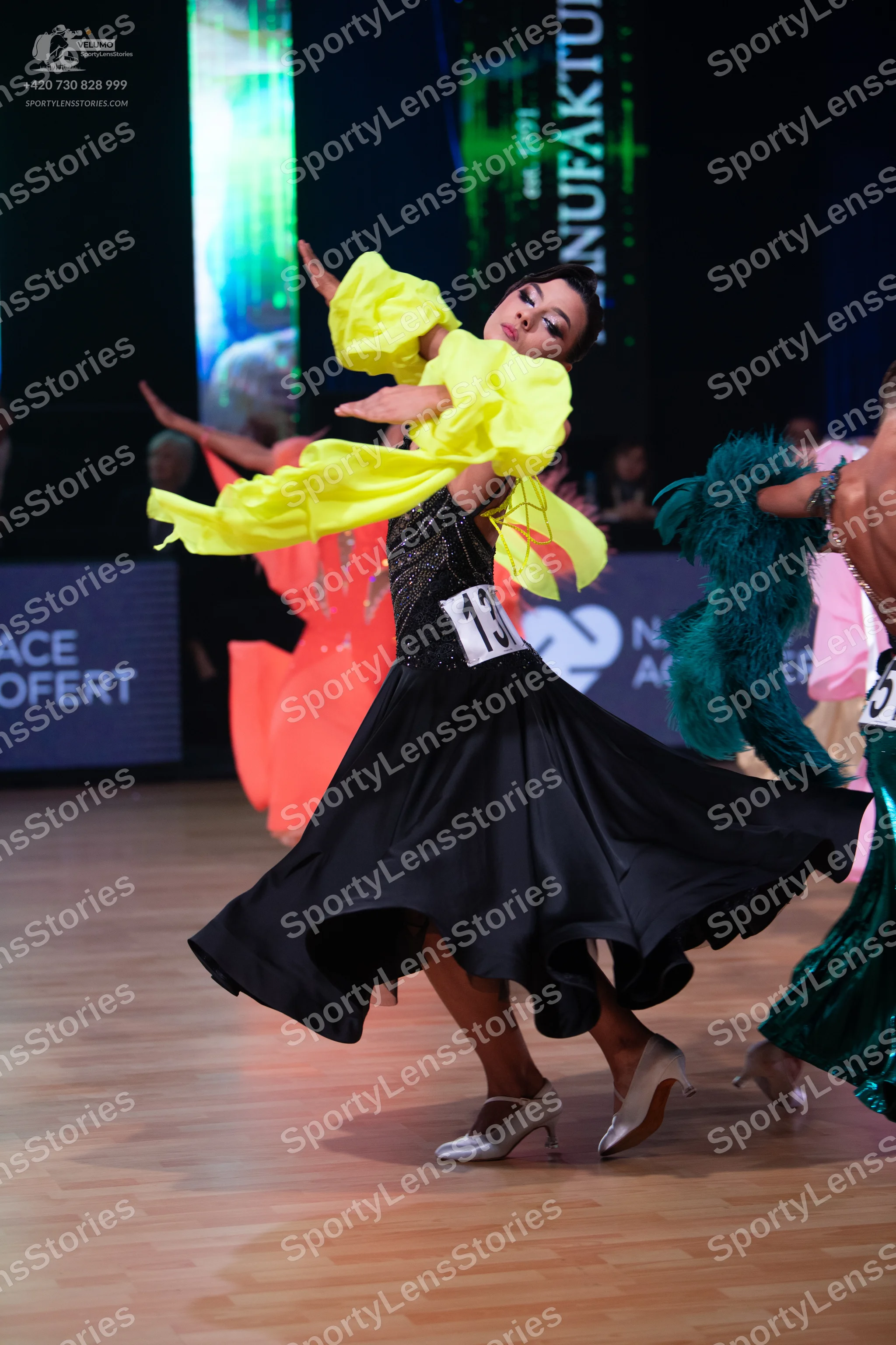 Dancesport competitor: Female dancer: black ballroom dress with a sequined bodice, a large black flowin