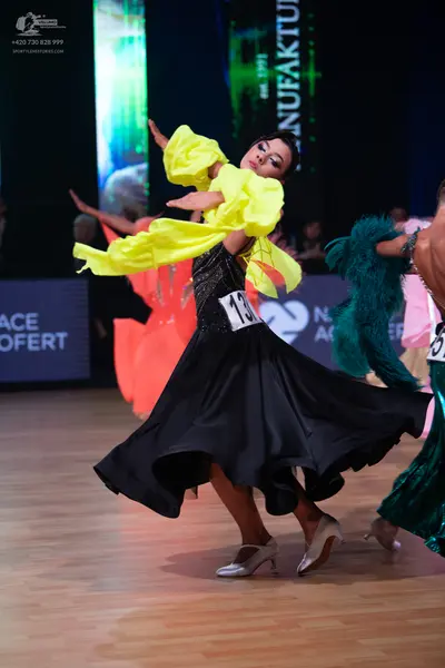 Dancesport competitor: Female dancer: black ballroom dress with a sequined bodice, a large black flowin