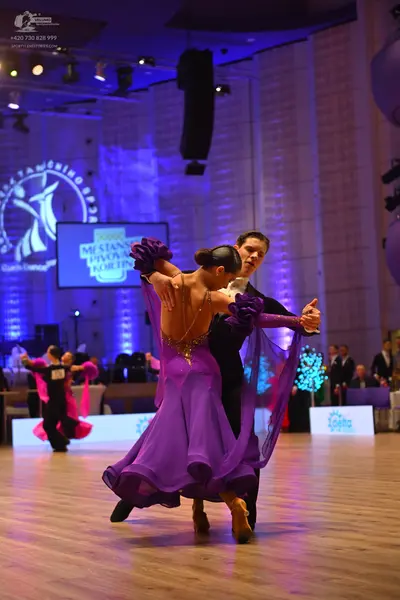 Dancesport competitor: Female dancer: purple ballgown with a flowing skirt and large purple floral acce