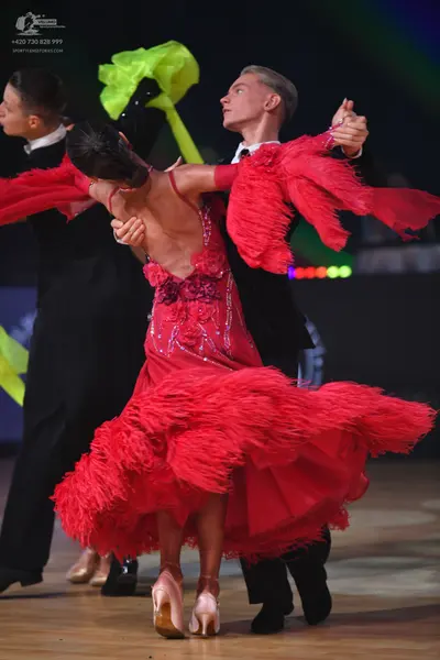 Dancesport competitor: Female dancer: red Latin dress with long fringe on the sleeves and skirt, featur