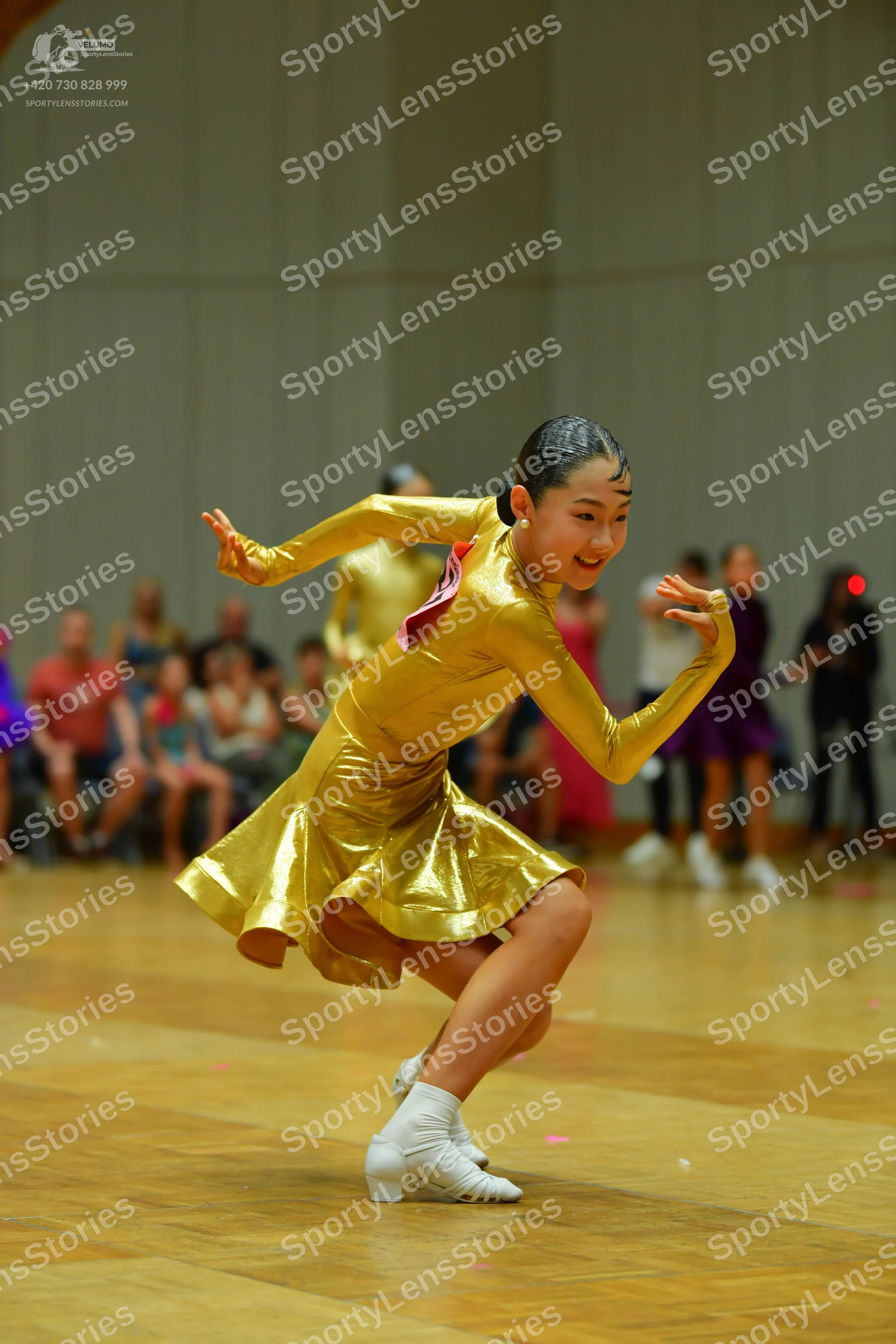 Dancesport competitor: Female dancer in foreground: gold metallic long-sleeved latin dress with a pink