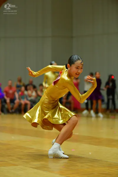 Dancesport competitor: Female dancer in foreground: gold metallic long-sleeved latin dress with a pink 