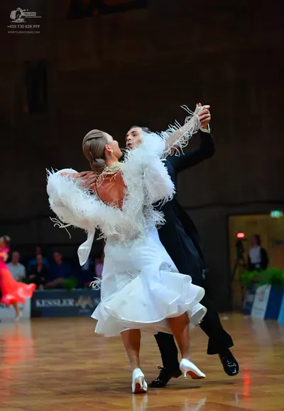 Dancesport competitor: Female dancer: white ballroom dress with a voluminous ruffled skirt and feather-