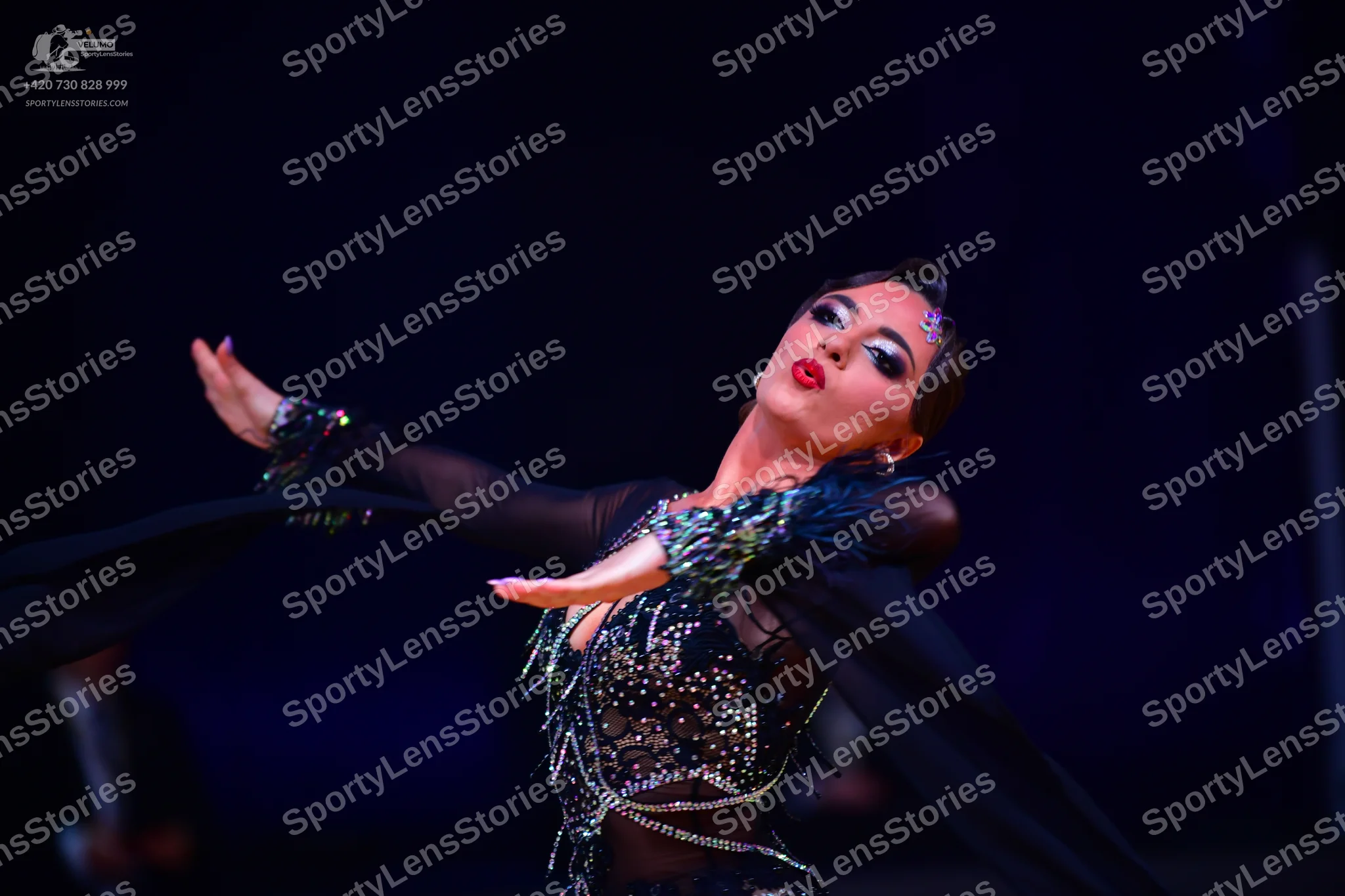 Dancesport competitor: Female dancer: black Latin dress with sheer sleeves, heavily embellished with rh