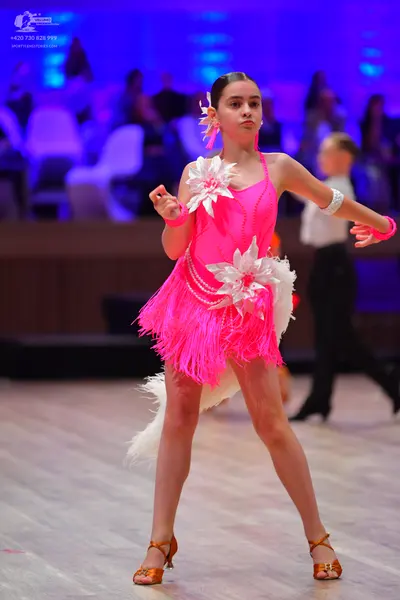 Dancesport competitor: Female dancer: bright pink latin dress with fringe and large white floral embell