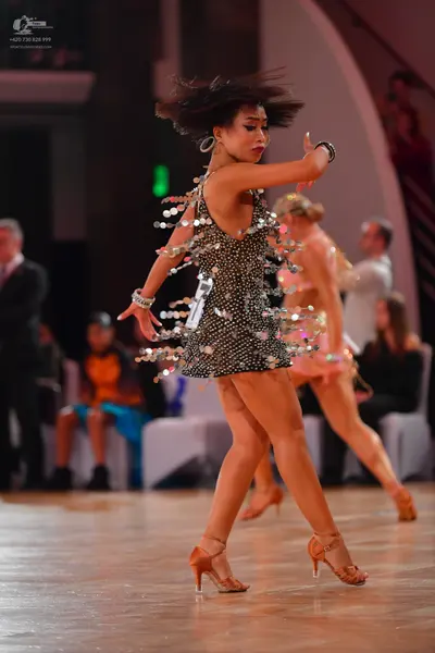 Dancesport competitor: Female dancer in foreground: black Latin dance dress heavily embellished with sm