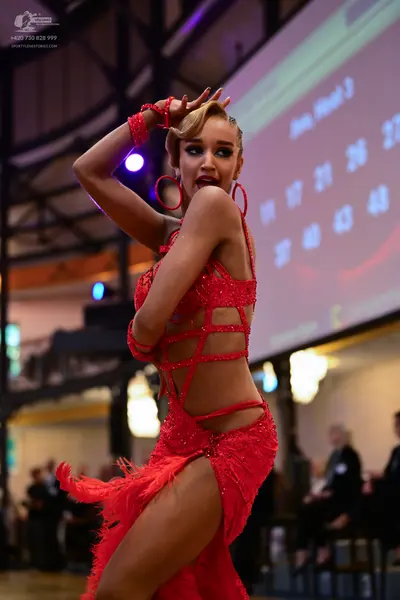 Dancesport competitor: Female dancer: red latin dress with sequins, cut-outs, and fringe, accompanied b