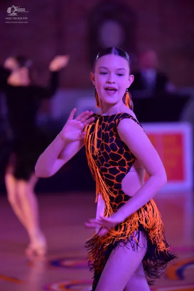Dancesport competitor: Female dancer in foreground: black Latin dress with orange leopard print and ora