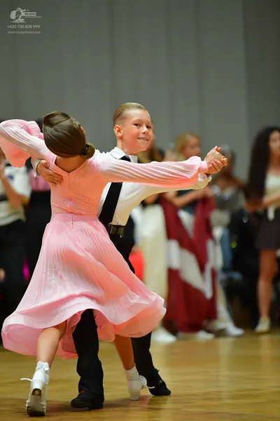 Dancesport competitor: Female dancer: light pink, long-sleeved, flowing dress with a pleated or chiffon
