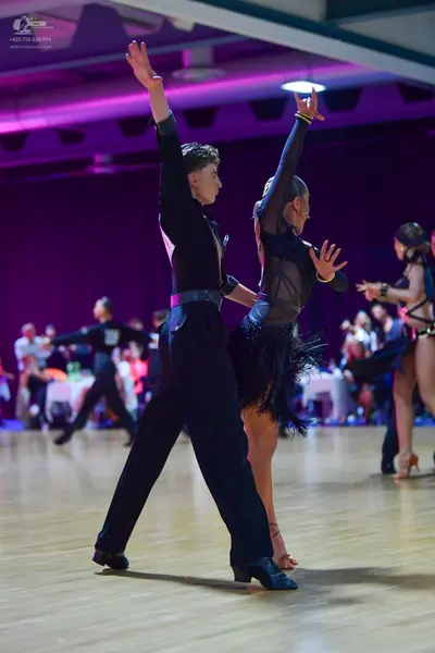 Dancesport competitor: Foreground male dancer: black long-sleeved shirt and black trousers