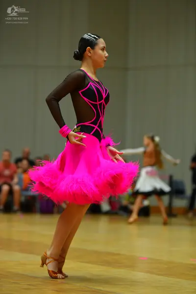 Dancesport competitor: Female dancer (foreground): black long-sleeved latin dress with bright pink pipi