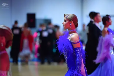 Dancesport competitor: Female dancer in foreground: blue Latin dance dress with sequins, feather accent