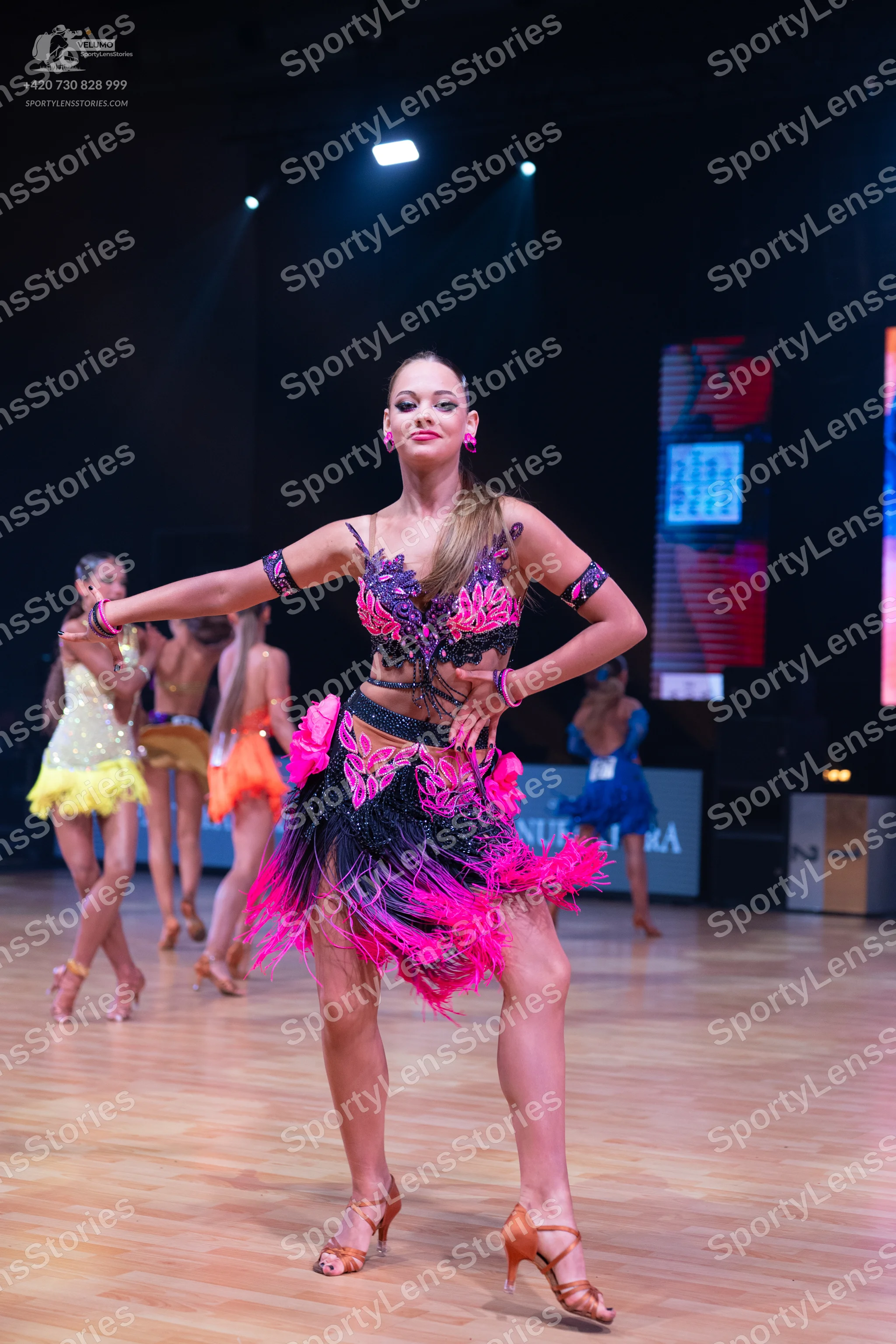 Dancesport competitor: Female dancer in foreground: black, purple, and bright pink Latin dance dress wi