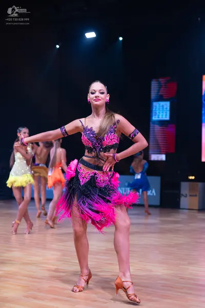 Dancesport competitor: Female dancer in foreground: black, purple, and bright pink Latin dance dress wi