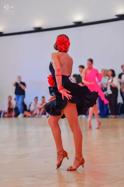 Dancesport competitor: Female dancer in foreground: black latin dress with a flared skirt, a large red 