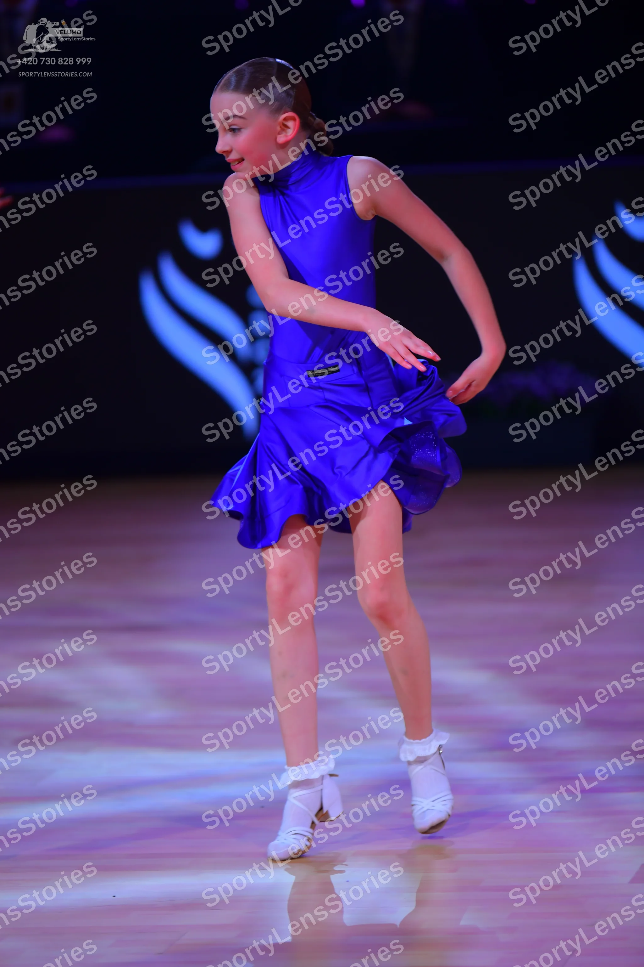 Dancesport competitor: Female dancer: blue, sleeveless, short satin-like dress with a ruffled skirt and