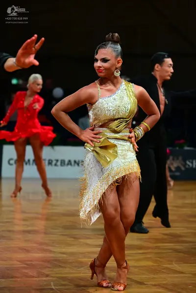 Dancesport competitor: Female dancer in foreground: gold and white asymmetric latin dress with sequins,