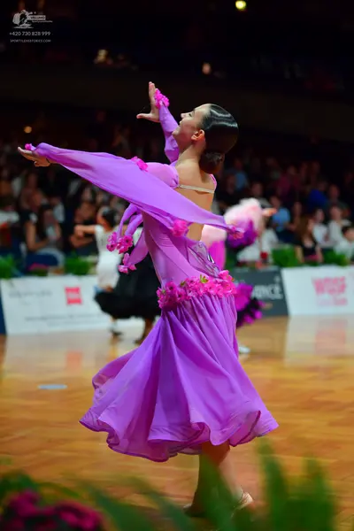 Dancesport competitor: Female dancer: purple Latin dance dress with long, flowing sleeves, decorated wi