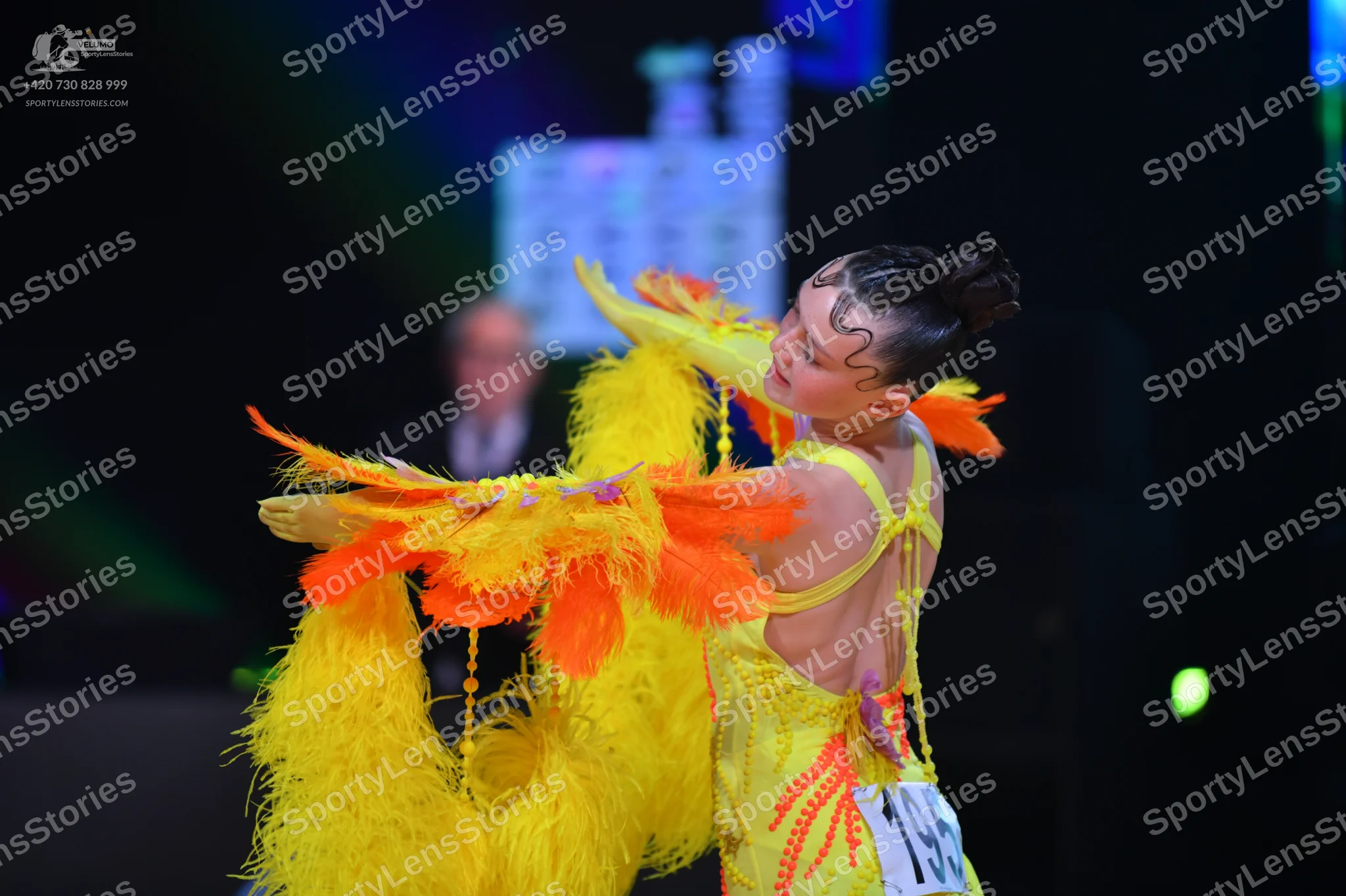 Dancesport competitor: Female dancer: bright yellow Latin dress with large yellow and orange feathers