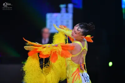 Dancesport competitor: Female dancer: bright yellow Latin dress with large yellow and orange feathers