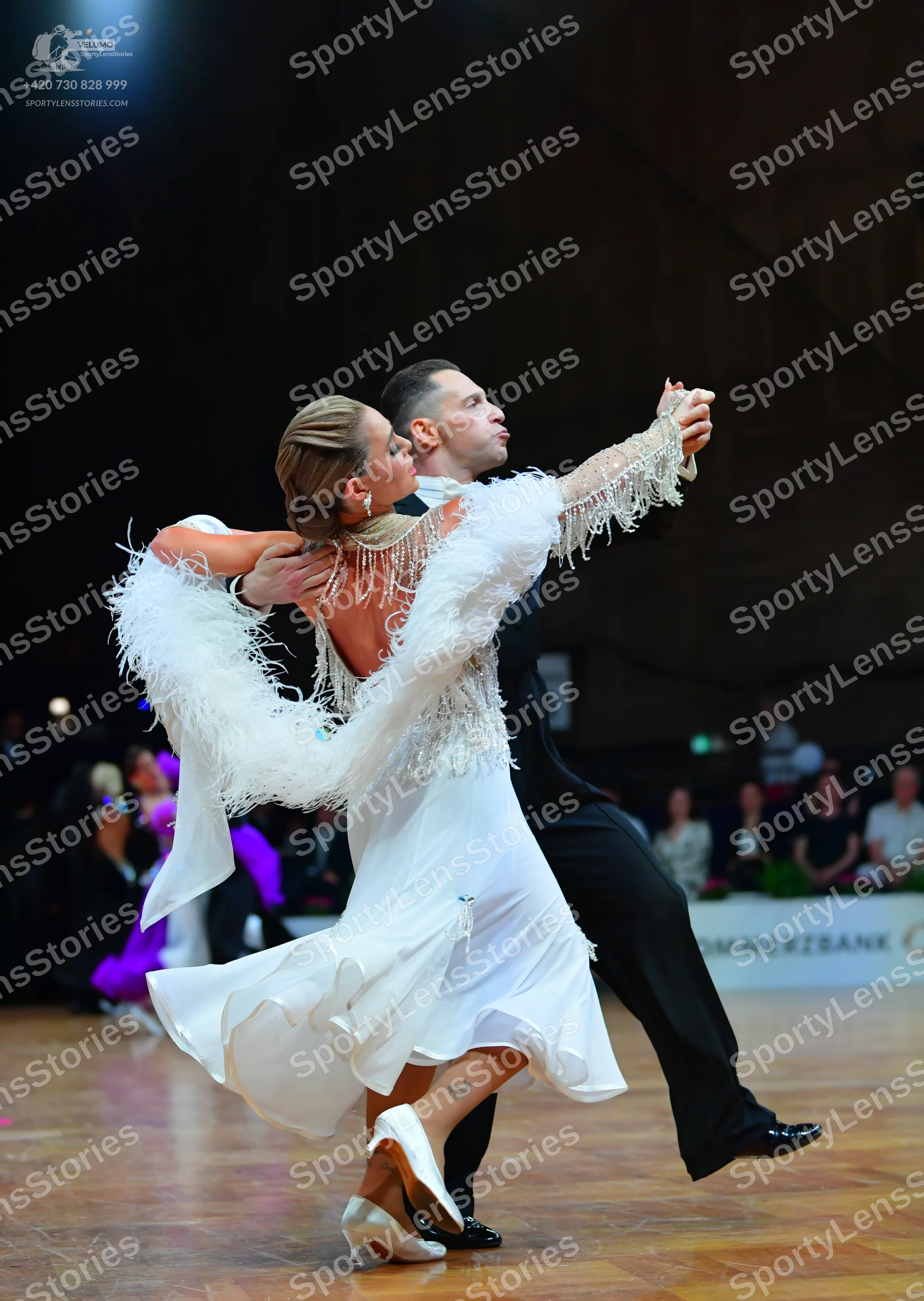 Dancesport competitor: Female dancer: white dance dress with large white feather/fringe trim on the sle
