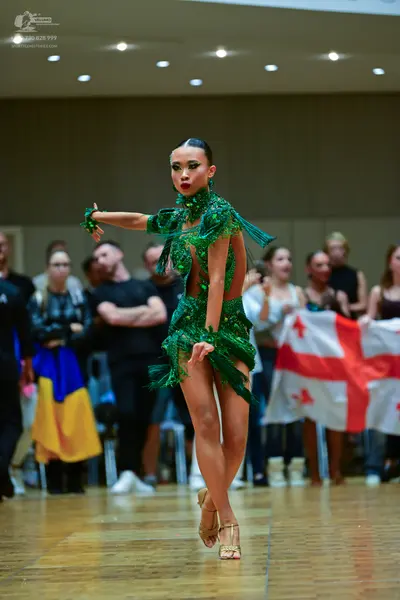 Dancesport competitor: Female dancer: emerald green Latin dress with long sleeves and extensive green f
