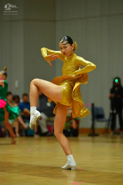Dancesport competitor: Female dancer in foreground: gold metallic long-sleeved Latin dance dress with a