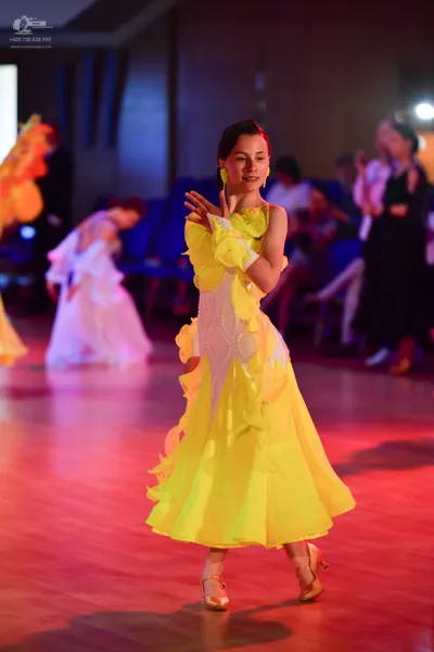 Dancesport competitor: Female dancer in foreground: bright yellow Latin dance dress with flowing ruffle