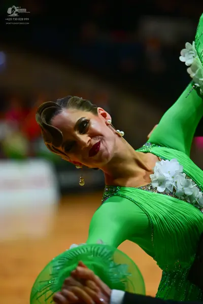 Dancesport competitor: Female dancer: bright green long-sleeved dress with white floral accents and tex