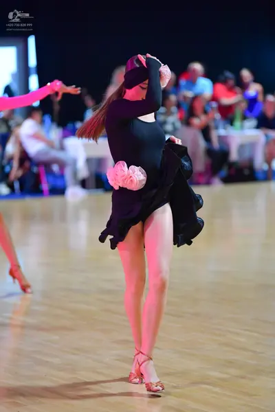 Dancesport competitor: Female dancer in center: black long-sleeved latin dress with large, pale pink/wh