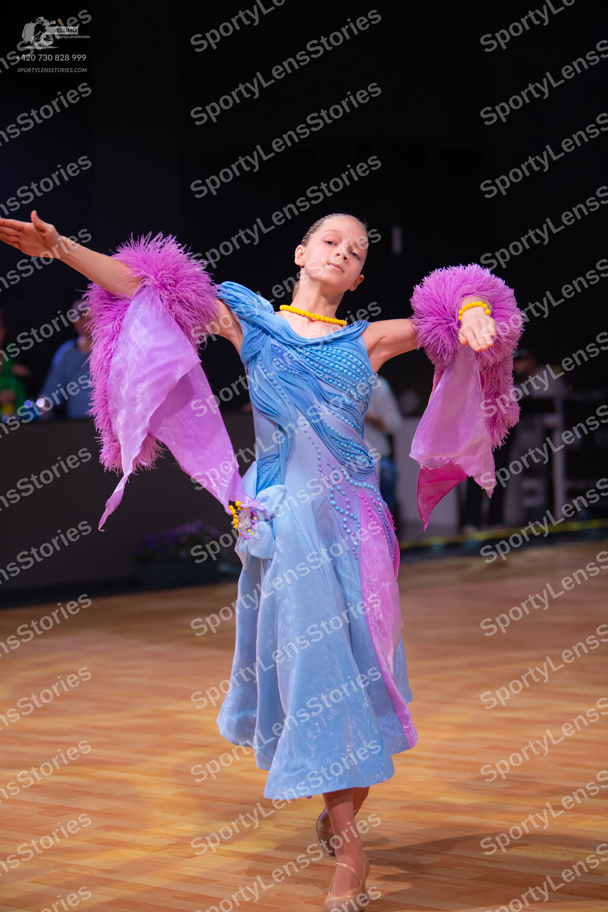 Dancesport competitor: Female dancer: light blue and pink Latin dance dress with feathery, fringed slee