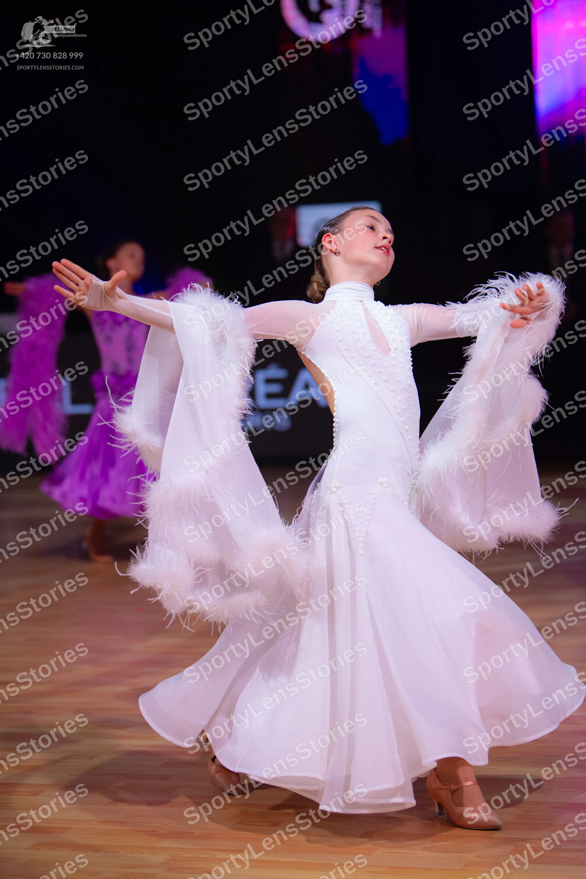 Dancesport competitor: Female dancer in foreground: white ballroom dress with a high neck, long sleeves