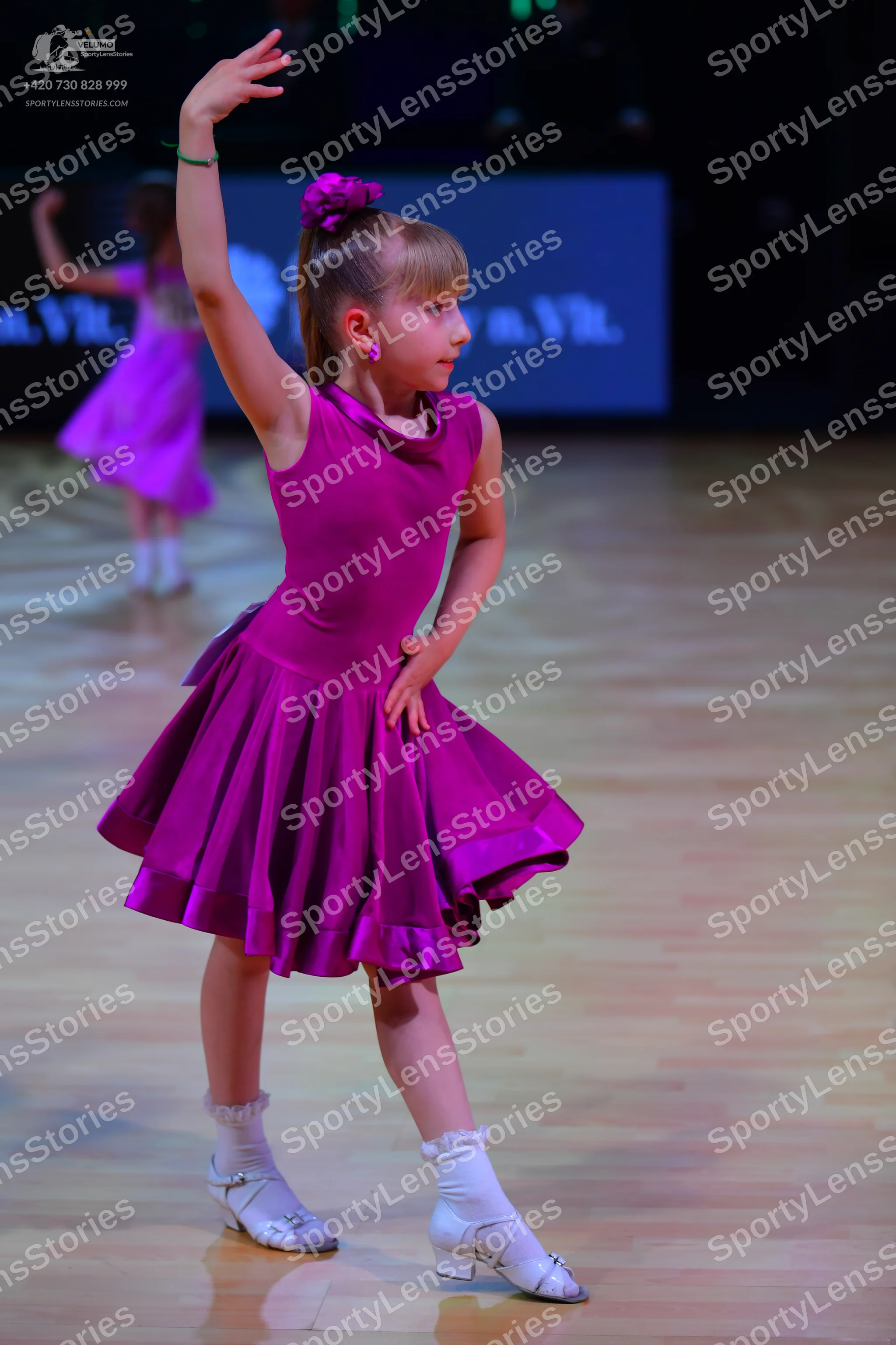 Dancesport competitor: Female dancer in foreground: purple sleeveless satin dress with a flared skirt,