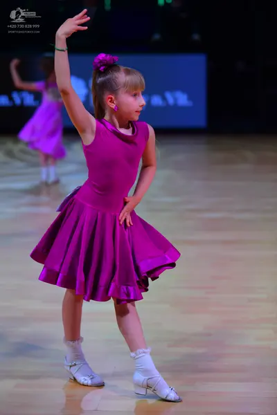 Dancesport competitor: Female dancer in foreground: purple sleeveless satin dress with a flared skirt, 