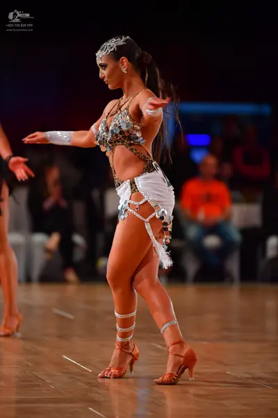 Dancesport competitor: Female dancer: silver, gold, and white Latin dance costume heavily embellished w