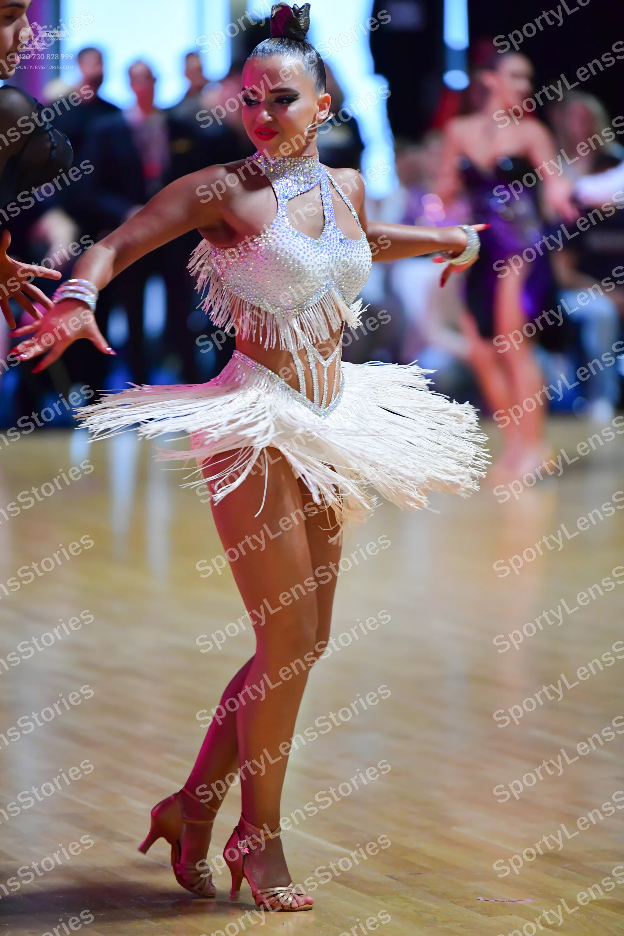 Dancesport competitor: Female dancer in foreground: silver sequin Latin dress with long fringe on the b
