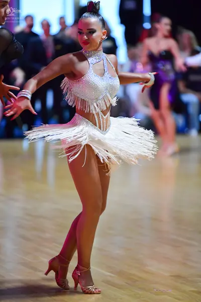 Dancesport competitor: Female dancer in foreground: silver sequin Latin dress with long fringe on the b
