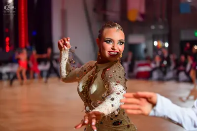 Dancesport competitor: Female dancer in foreground: nude-colored, long-sleeved dance dress with heavy s