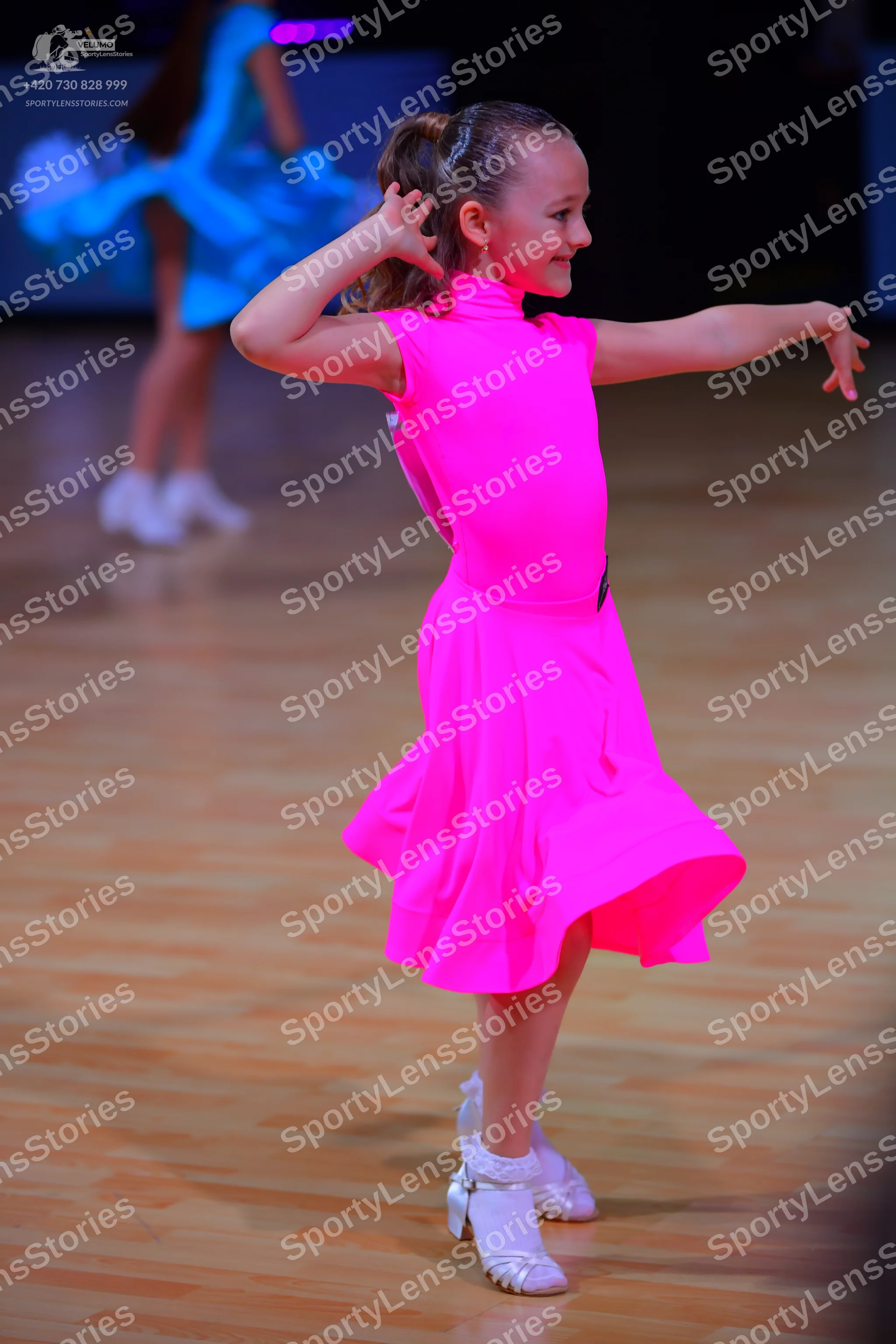 Dancesport competitor: Female dancer in foreground: bright neon pink sleeveless Latin dress with a flar