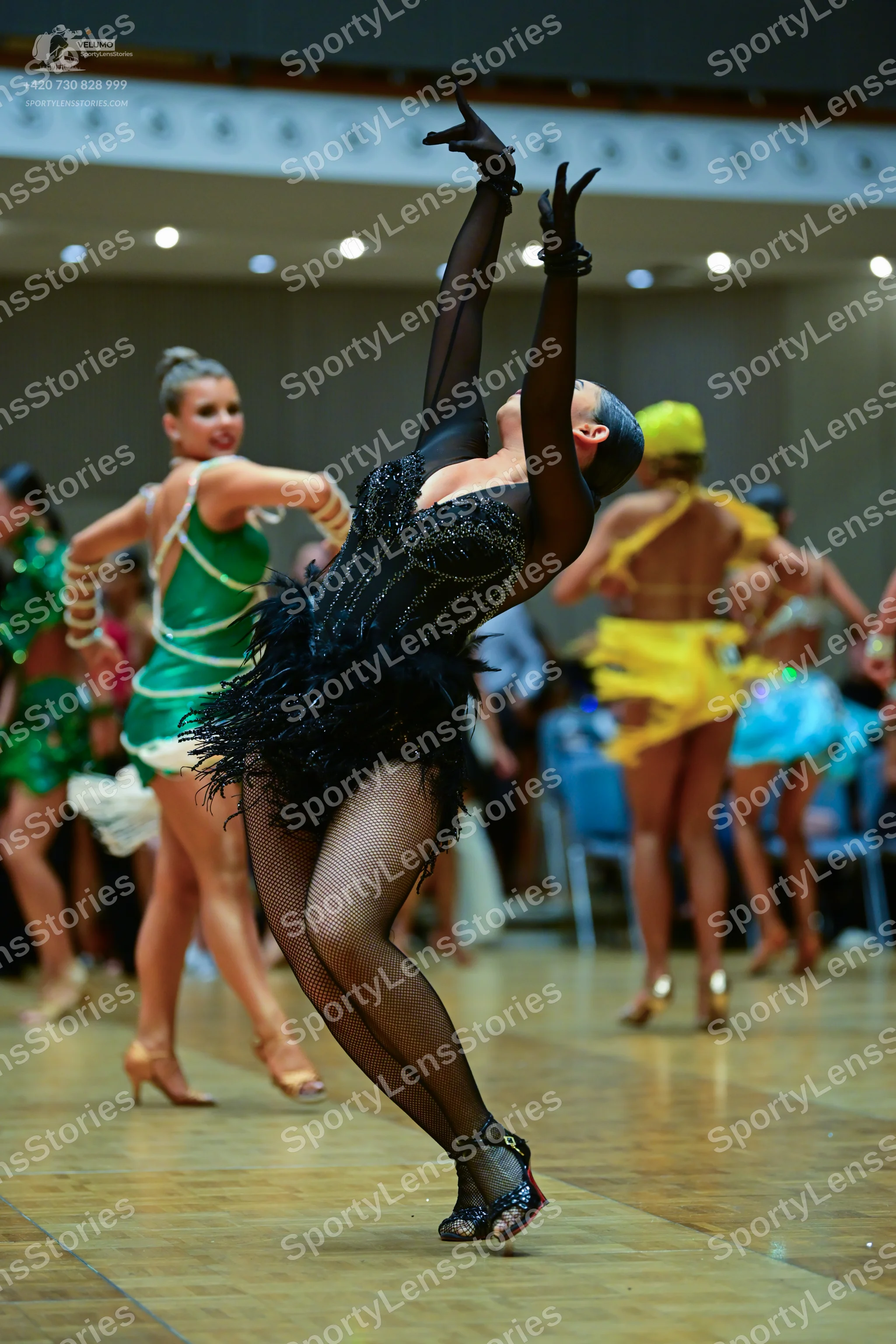 Dancesport competitor: Female dancer in foreground: black latin dress with a sequined bodice, mesh slee