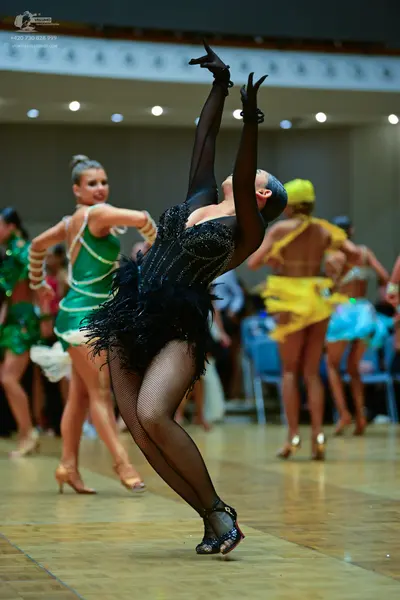 Dancesport competitor: Female dancer in foreground: black latin dress with a sequined bodice, mesh slee