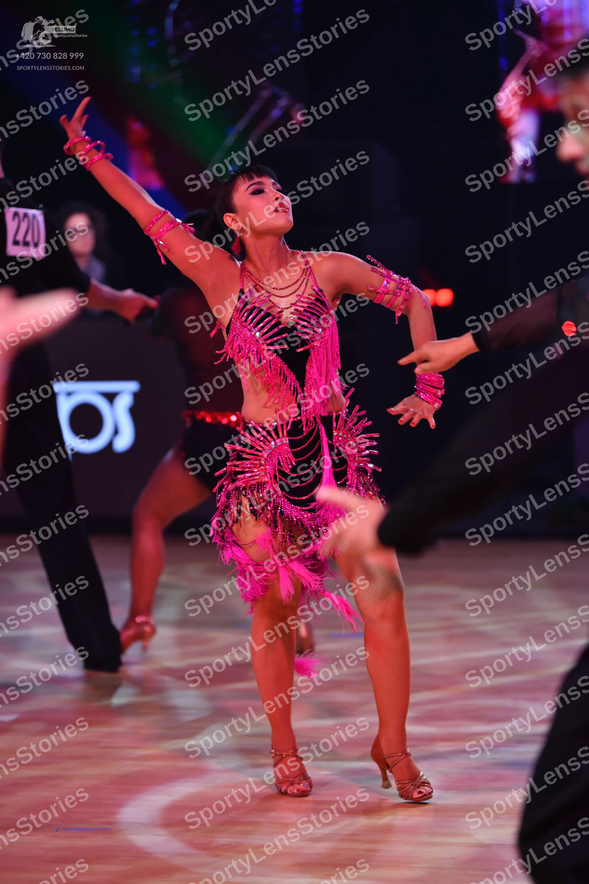 Dancesport competitor: Female dancer in foreground: pink latin dress with sequins and long fringe, with