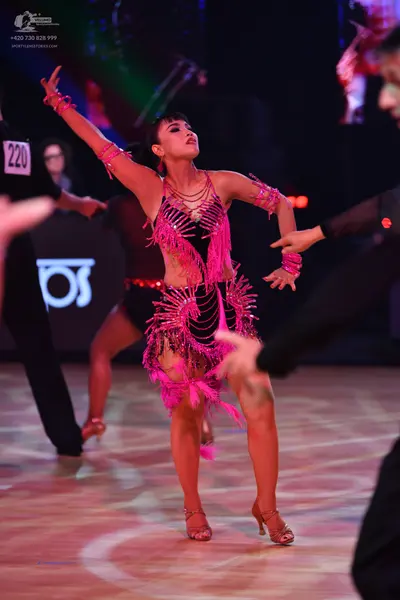 Dancesport competitor: Female dancer in foreground: pink latin dress with sequins and long fringe, with