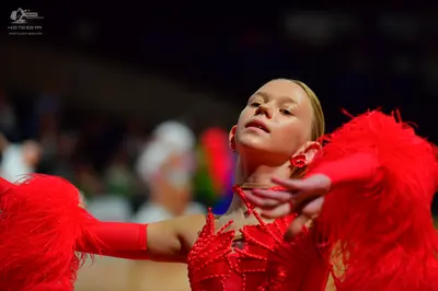 Dancesport competitor: Female dancer: red latin dress with large red feather-like fringes on the sleeve