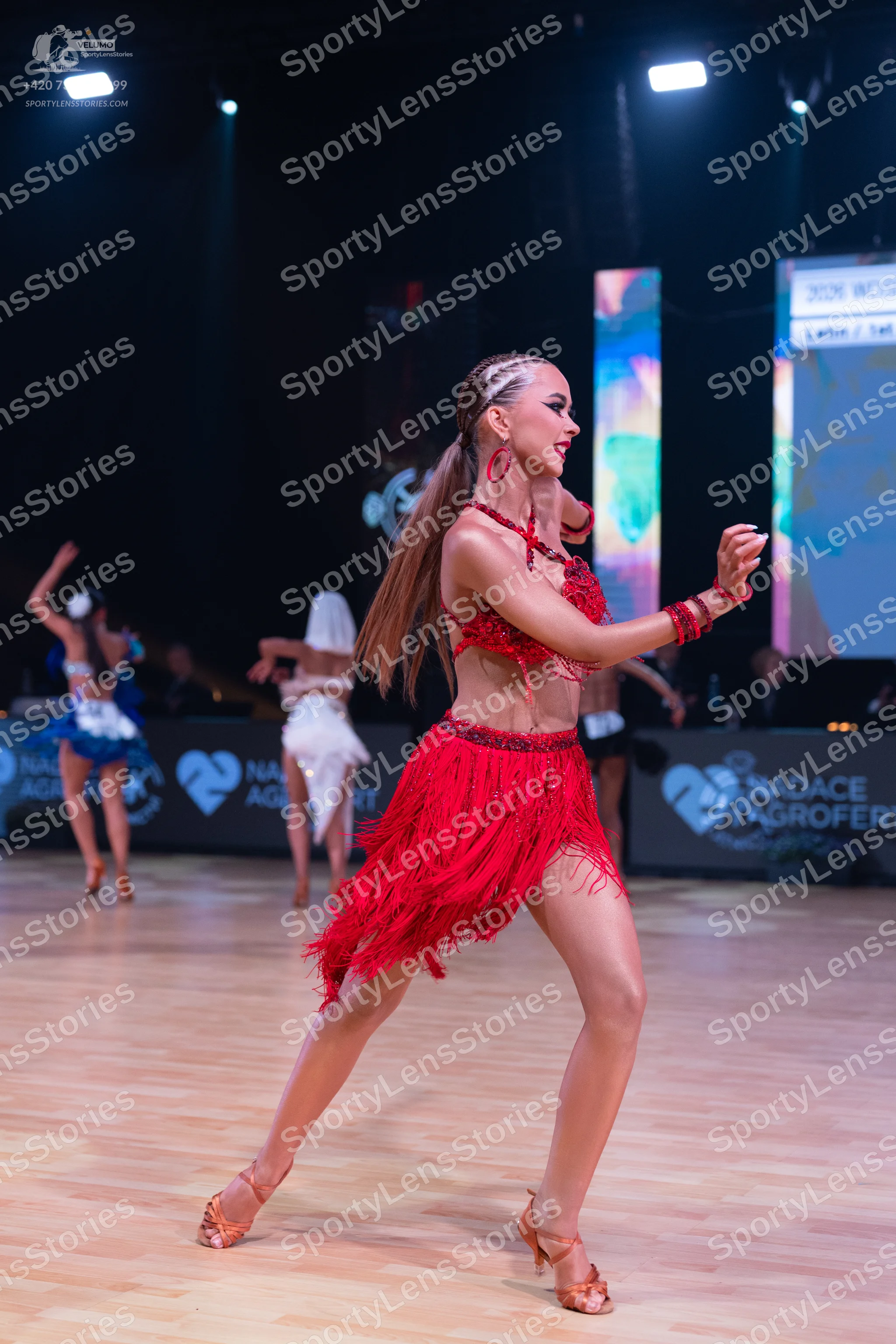 Dancesport competitor: Female dancer in foreground: red latin dress with long fringe, red earrings, and