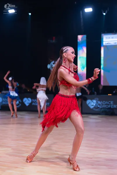 Dancesport competitor: Female dancer in foreground: red latin dress with long fringe, red earrings, and