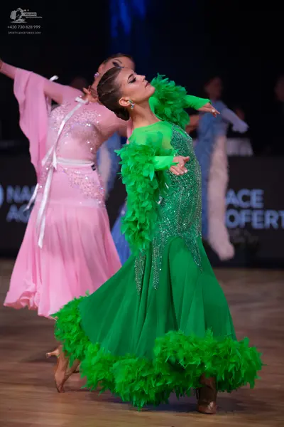 Dancesport competitor: Female dancer in foreground: bright green standard dance dress with a sequined b